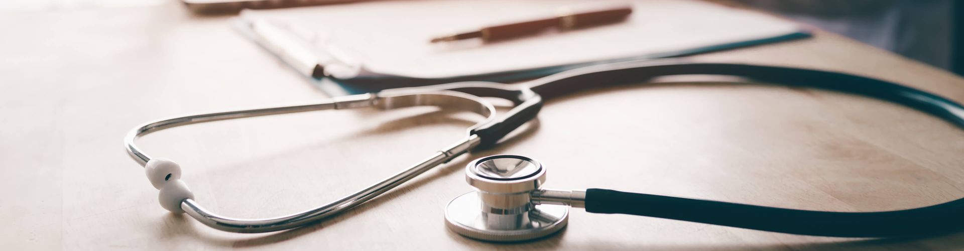 Ein Stethoskop und ein Stift liegen auf einem Schreibtisch.